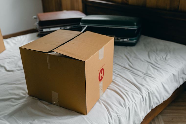 Carton de déménagement posé sur un lit, valises derrière