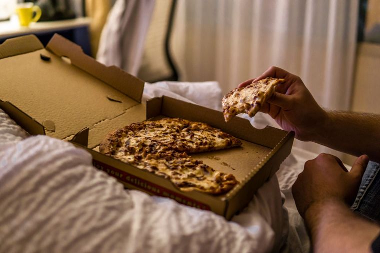 Part de pizza mangée au lit, boîte en carton sur la couette