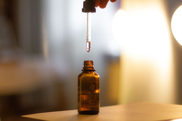 Compte-gouttes au-dessus d'un flacon ambré d'huile essentielle, en contre-jour