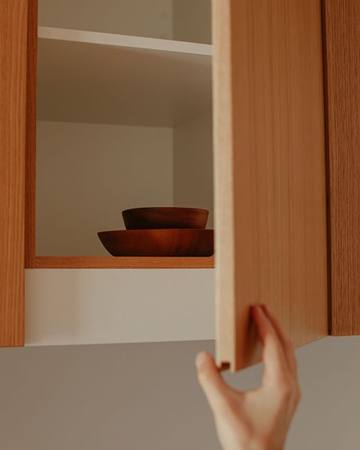 Main ouvrant un placard de cuisine en bois