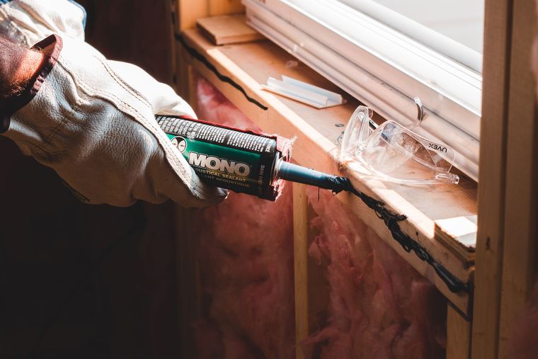 Ouvrier ganté appliquant un joint de mastic sur un encadrement de fenêtre