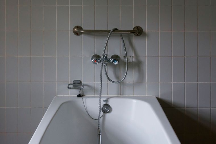Baignoire encastrée contre un mur carrelé, robinet et douchette