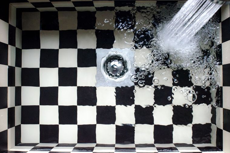 Bonde d'évacuation vue de dessus sur un carrelage en damier, l'eau s'y écoule