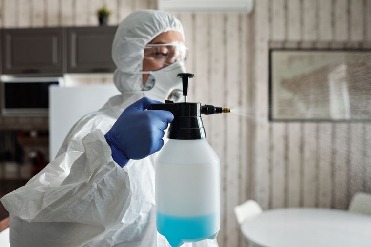 Technicien ganté tenant un pulvérisateur à main, en tenue de protection